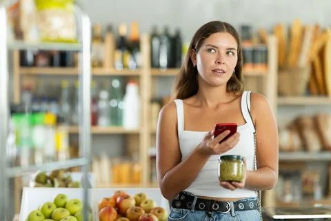 Female shopper scans QR code on green peas jar label using smartphone. Checking Stock-Fotos