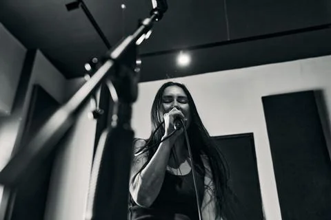 Female singer performs into microphone during studio rehearsal under moody .. Stock Photos