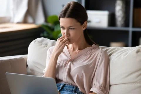 Female sitting on couch looking at computer screen feels confused Foto stock