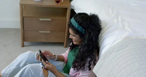 Female sitting on floor by bed, bringing smartphone up, scrolling and tapping Stock Footage 337098894