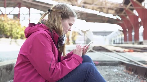 Female sitting on railroad tracks texting on cell phone 4k Stock Footage