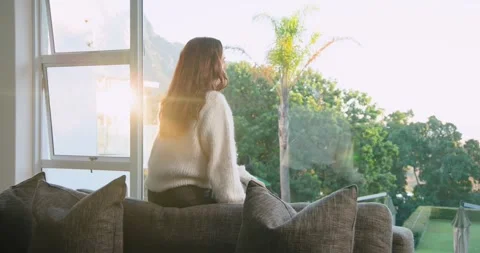 Female sitting on sofa back by window, adjusting, turning to camera reacting to Stock Footage 341953856