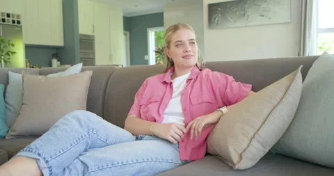Female sitting on sofa, glancing at window, adjusting pillow, leaning back, Stock Footage 337294559