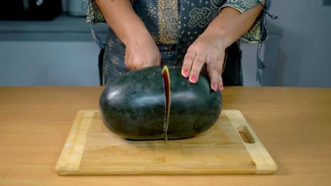 Female slicing a fresh watermelon with a sharp knife in the kitchen Video stock 158415049