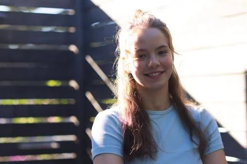 Female smiling and posing in backyard by slatted fence with sunlit wall, Stock Photos