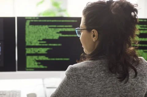 Female software developer coding at computer with dual monitors in modern office Foto stock