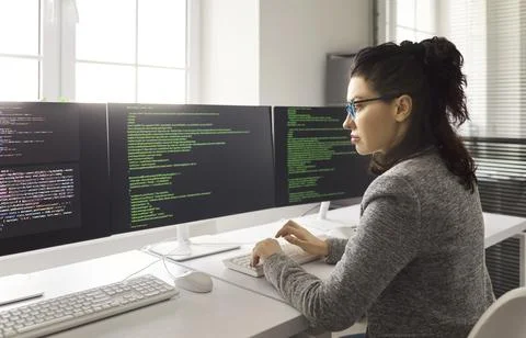 Female software developer coding at multi monitor workstation in modern office Stock Photos