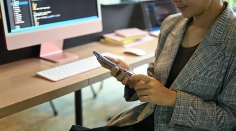 Female software developer using mobile phone, sitting office desk with Stock Photos