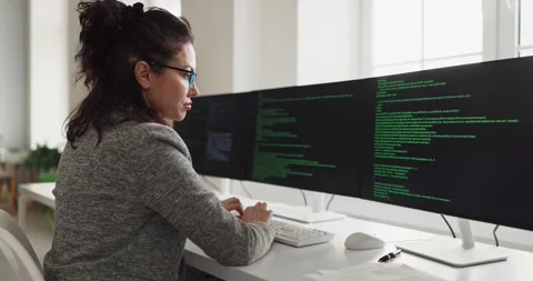 Female software engineer coding at multi monitor workstation in modern office Vídeo Stock 337810925