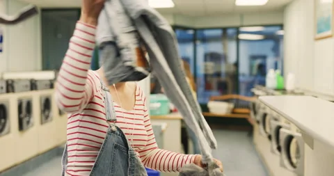 Female sorting through her clothing to put in a washing machine in interior smal Stock Footage 199459892
