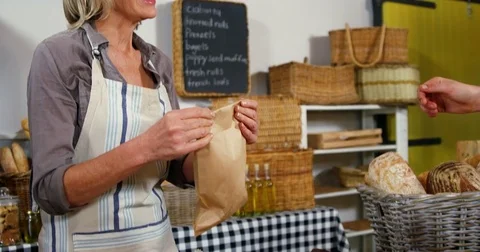 Female staff giving packed bread to woman at bakery section Stock Footage 72328843