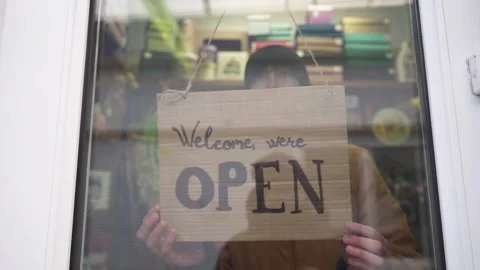 A female store manager changes the Closed to Open sign on the window. Small Stock Footage 263890383