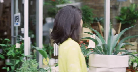 Female store owner going outside boutique flower shop to water plants in exterio Stock Footage 199455277