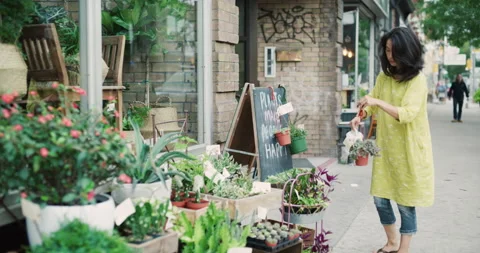 Female store worker going outside boutique floral shop to water plants in exteri Stock Footage 199462315