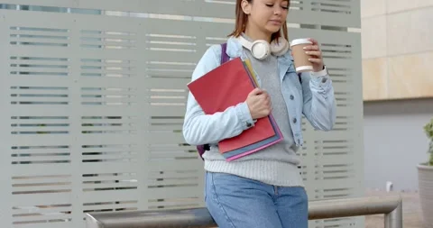 Female student approaching railing at building, leaning and sipping coffee while Stock Footage 345070603
