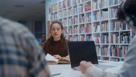 Female student with dreadlocks reading a book in a library 스톡 동영상 335125666