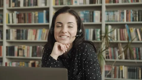 Female student with a headset, sitting at a table in the library, holding a Stock Footage 154277705