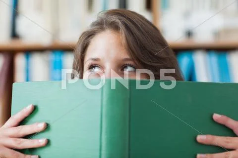 Female student holding book in front of her face in library Stock Photos