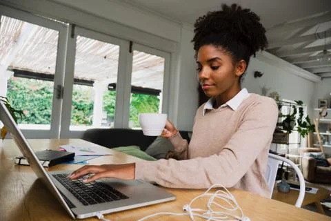 Female student making notes typing on laptop holding hot coffee sitting in fancy Stock Photos