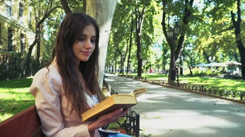 Female student reading a book on a bench in park Stock Footage 56936660