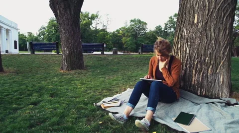 Female student sitting under a tree in park and using tablet Stock Footage 54515174