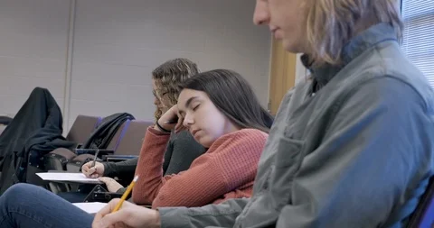 Female student sleeping in class while her classmates work on their assignments Видео 105910131