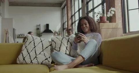 Female Student on Sofa looking at Smart phone in Warehouse conversion Stock Footage 237740553