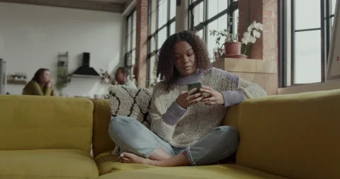 Female Student on Sofa looking at Smart phone in Warehouse conversion Stock Footage 237741345