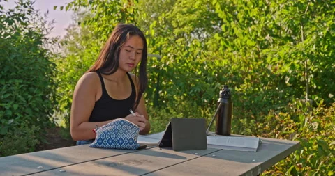 Female student studying class materials in a park. Vídeos de archivo 331090267
