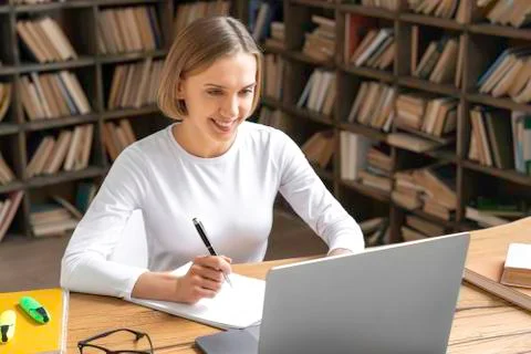 Female student is studying in a library using a laptop. Stock Photos