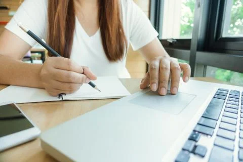Female student taking notes from a book at library. Stock Photos