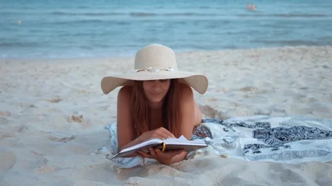 Female student uses vacation to study while reading book on beach near turquoise Stock Footage 275870090