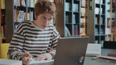 Female Student Using Laptop and​ Writing Notes in Library Stock Footage 277700519