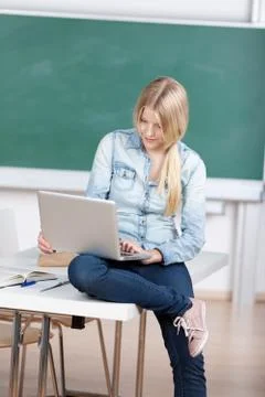 Female student using laptop while sitting on desk 写真素材