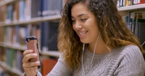 Female student using a mobile phone to video chat with headphones in a library Stock Footage 104809417