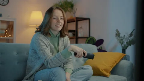 Female student watching TV program at night using remote control enjoying Video stock 166828415