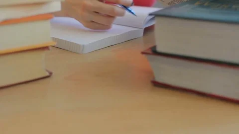 Female student writes in exercise book, doing homework, piles of books close up Stock-Footage 75171006