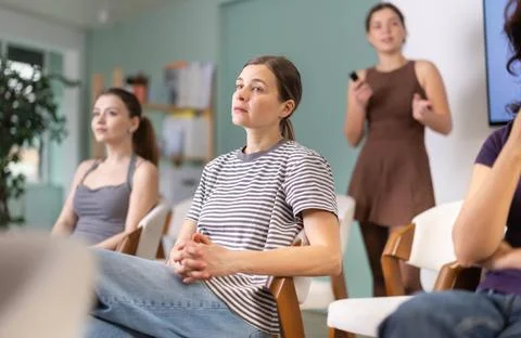Female students are sitting in study room. Coach speaker telling in background. Stock Photos