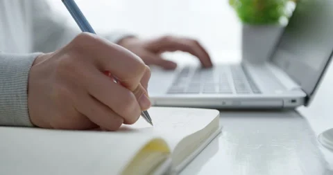 Female student's cropped hands write with a pen in a notebook and use a laptop  Stock Footage 152232580