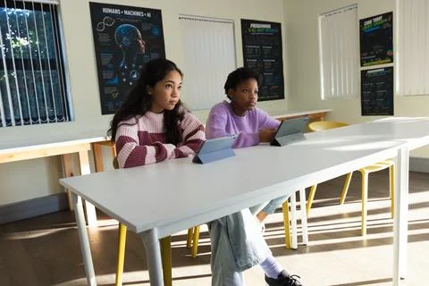 Female students sitting at table in classroom using tablets near Humans + Stockfoto's