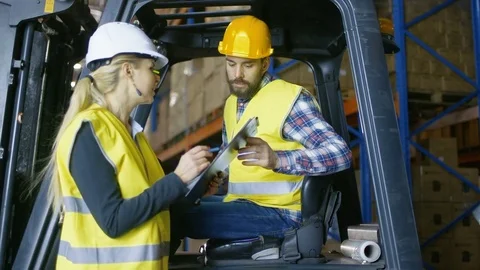 Female Supervisor Gives Work Assignment to Forklift Driver. They're in Warehouse Stock Footage