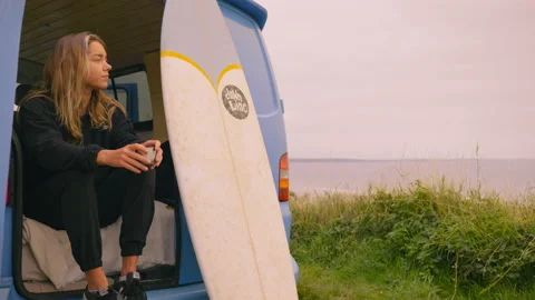 Female surfer sits in van drinking coffee overlooking the sea 스톡 동영상 160413017