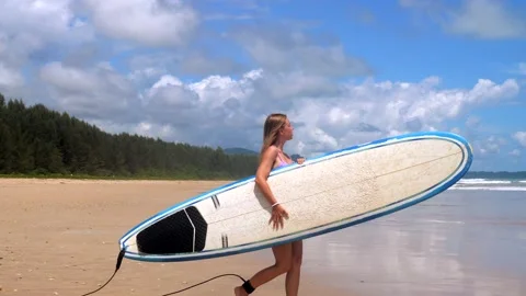 Female surfer walking with board on empty sandy beach. Young woman with Stock Footage 200825094