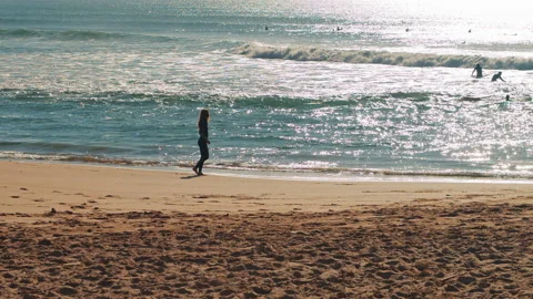 Female surfer walking down the Atlantic Ocean beach at sunset. Stock Footage 130628550