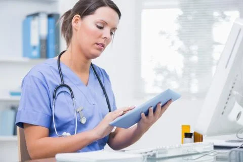 Female surgeon using digital tablet in front of computer at clinic Stock Photos