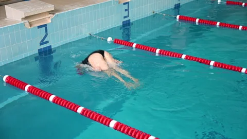 Female swimmer executes backstroke flip turn in indoor pool lane. Dynamic Stock Footage 346545816
