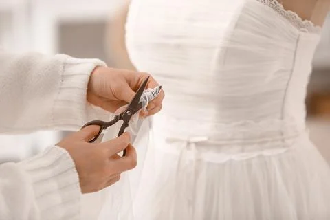 Female tailor's hands with scissors fitting wedding dress on mannequin in ate Stock Photos