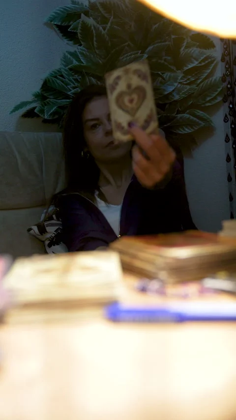 Female tarot reader at desk under glowing gourd lamp for spiritual guidance 스톡 동영상 333571657