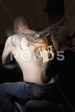 A Female Tattoo Artist Tattooing A Man's Back In A Tattoo Shop