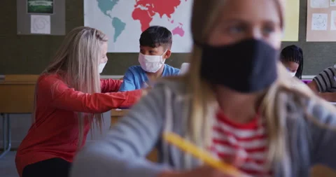 Female teacher and boy wearing face mask using laptop in class at school Stock Footage